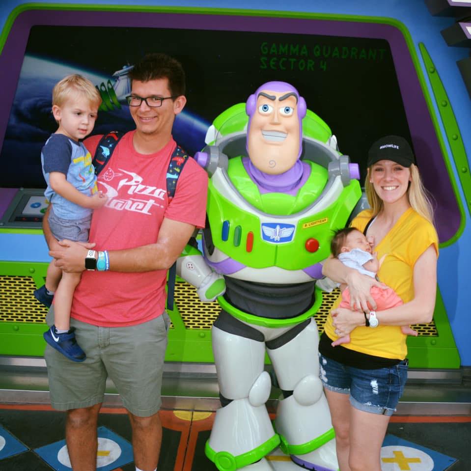 Melissa and Jordan Allen holding a toddler son and baby girl taking a photo with Buzz Light-year