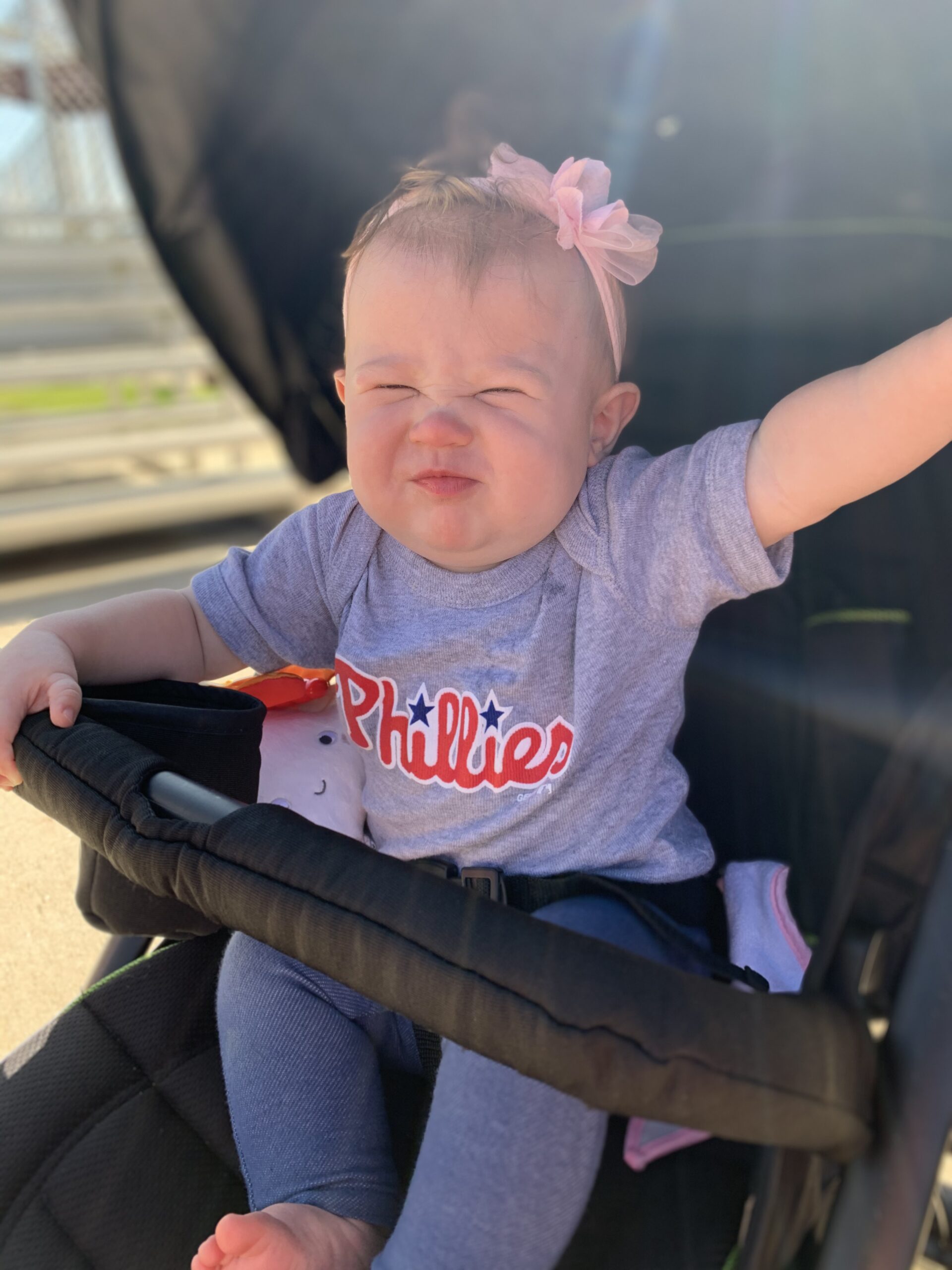 baby in stroller scrunching her face with a pink headband and a Phillies shirt