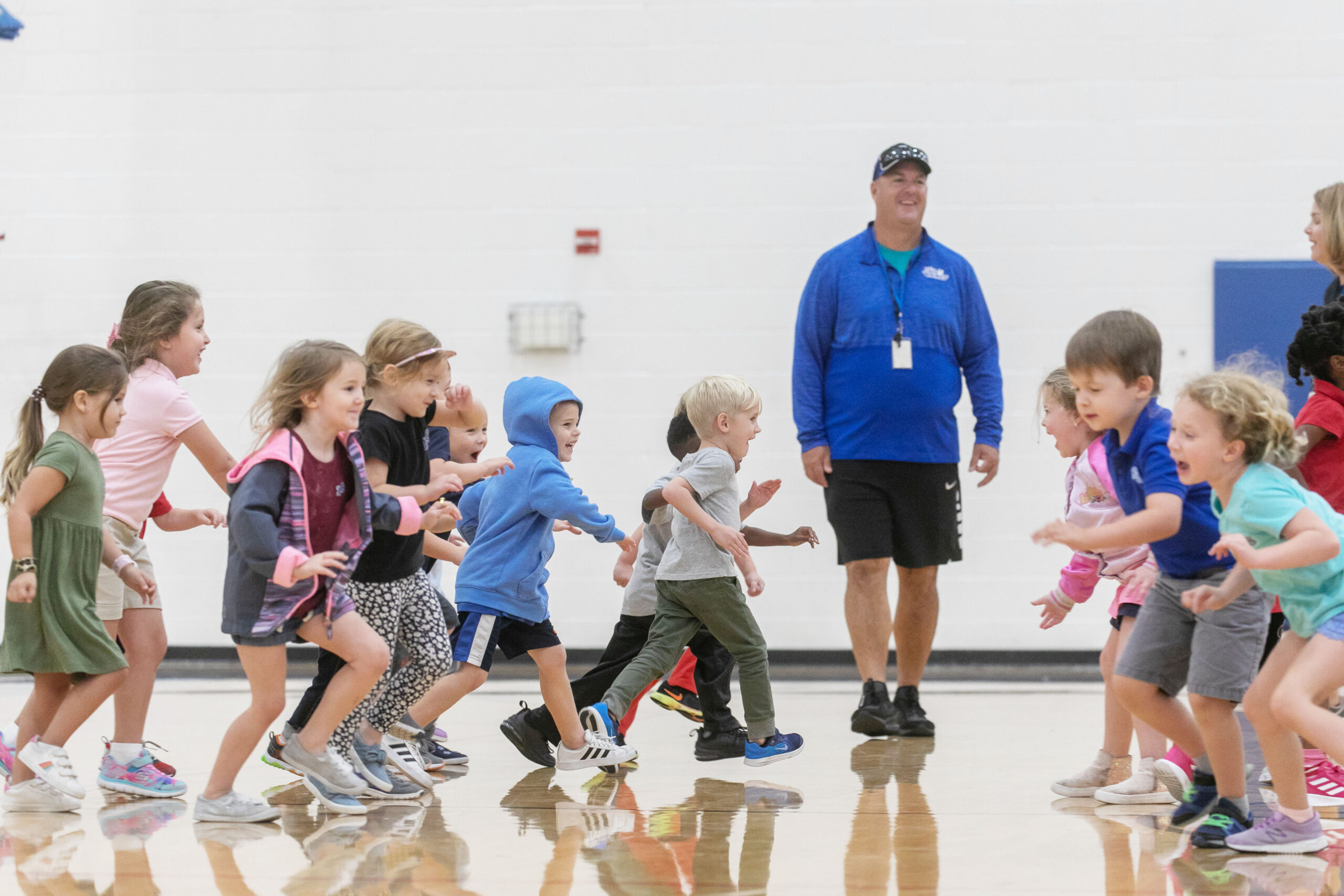 mike carl in the gym with several elementary children running around the gym