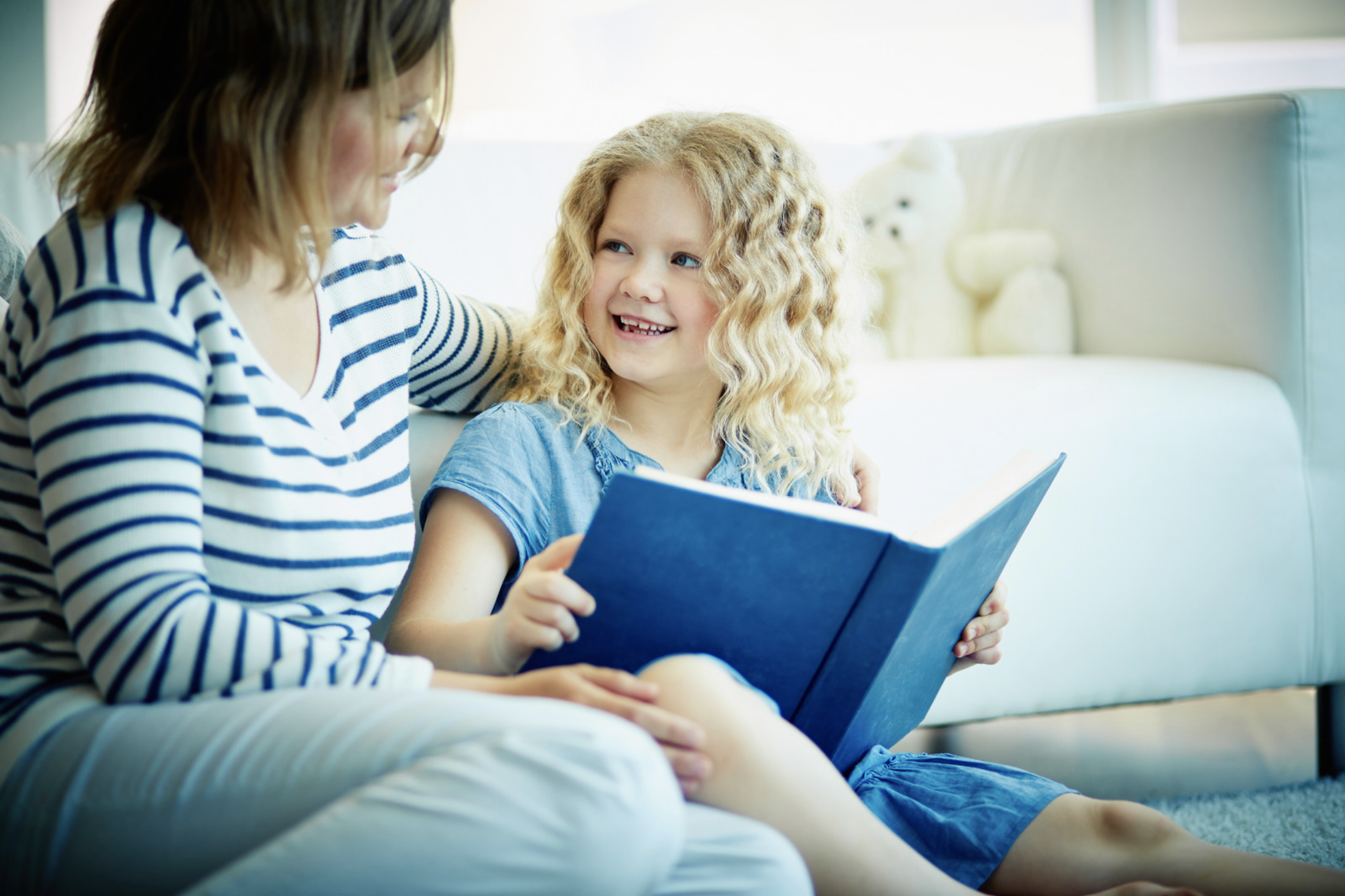 mother and daughter sitting together with a book. Daughter is looking at mother with a smile