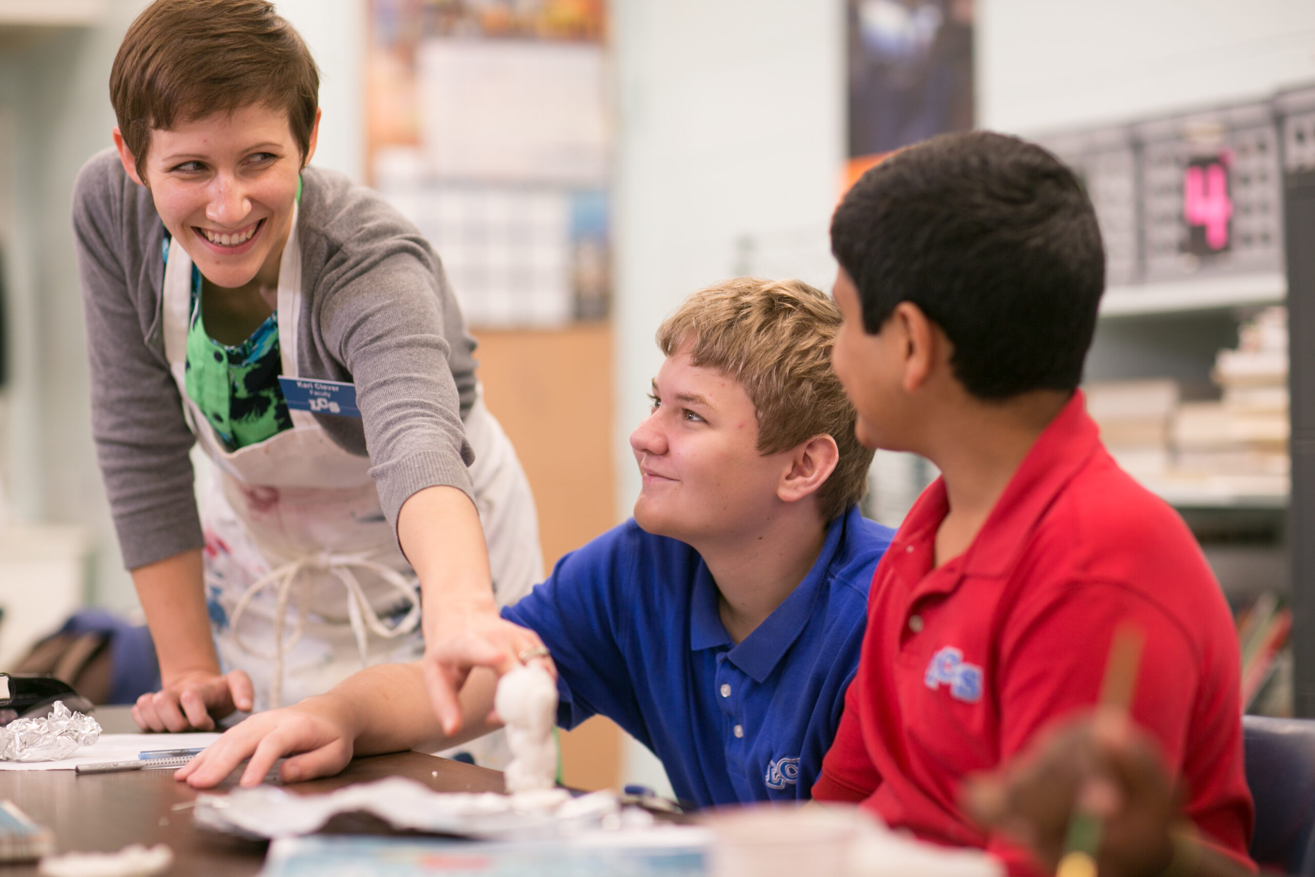 art teacher, Kari clever assisting students in an art class with two students pictured
