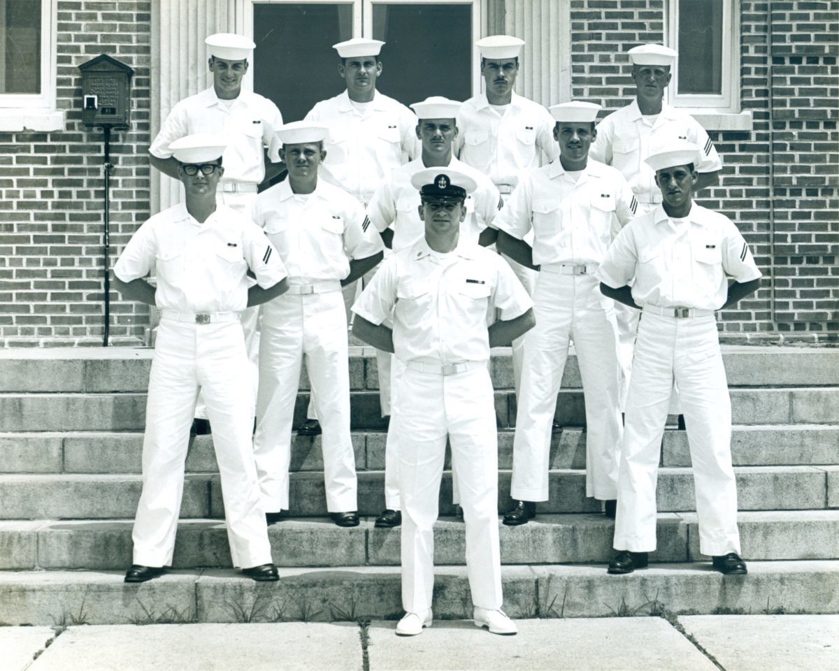 ten USS rangers dressed in white uniforms at attention on the front steps of a brick building